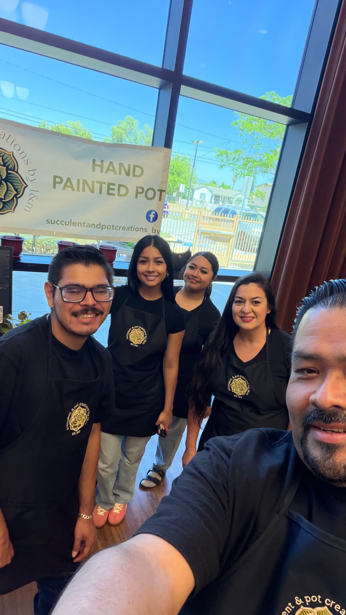 Five smiling people wearing black aprons pose for a selfie at a succulent business.