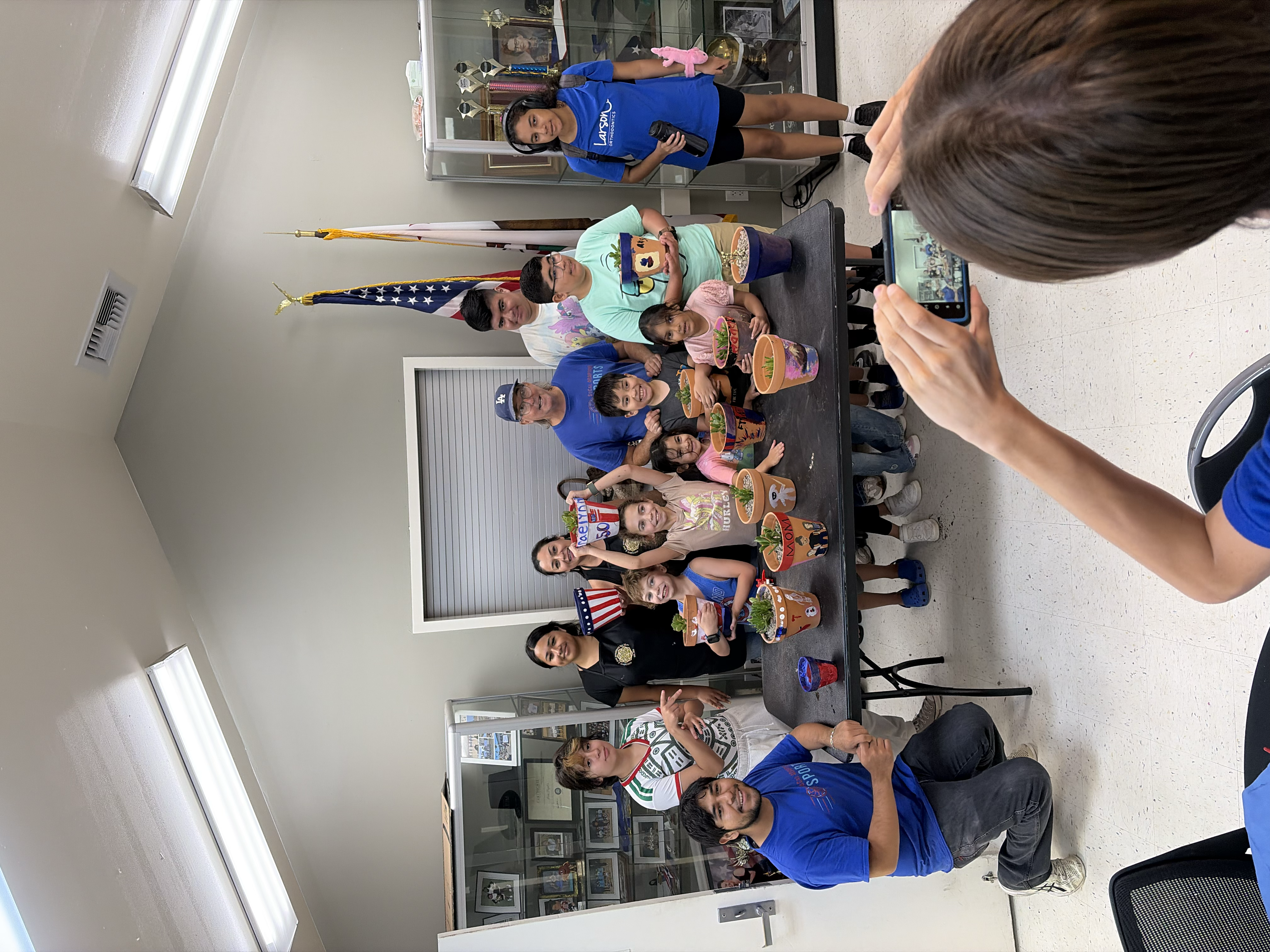 Diverse group of children and adults posing with hand-painted succulent pots for a photo.